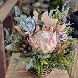 Winter floral arrangement with protea, succulents, and pinecones in a bowl vase