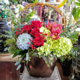 Red roses and pink orchids in a dark vase with a woven handle