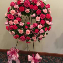 Pink and red floral wreath on a stand with ribbon bows