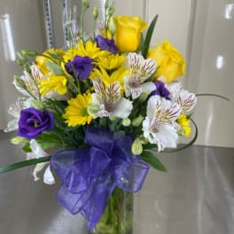 Bouquet of yellow roses, purple lisianthus, and white alstroemeria in a glass vase