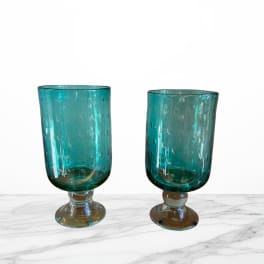 Two teal glass goblets with short stems on a white surface