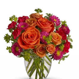 Orange roses and magenta daisies in a clear glass vase