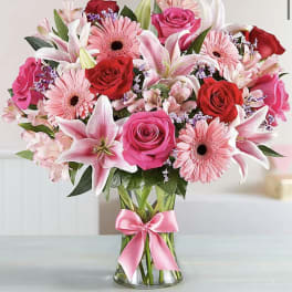Bouquet of pink and red flowers in a clear glass vase with a pink ribbon
