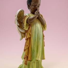 Praying angel figurine in a green and gold robe on a pink background