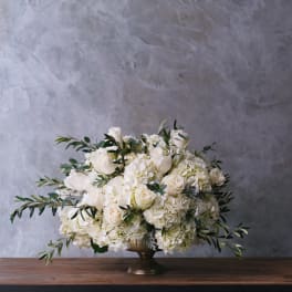 White rose and hydrangea arrangement in a gold pedestal vase