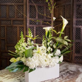White floral arrangement with calla lilies and hydrangeas in a white rectangular vase