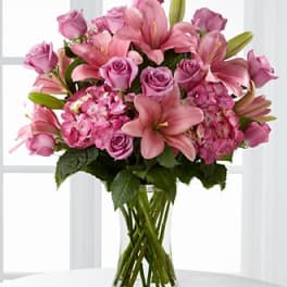 Pink lilies and roses arranged in a clear glass vase