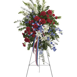 Standing floral spray with red carnations, white lilies, and blue accents