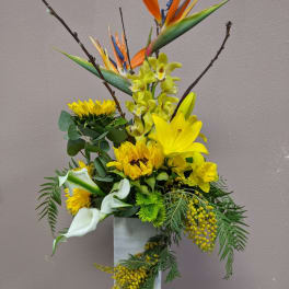 Tall floral arrangement with yellow blooms, white calla lilies, and bird of paradise in a white vase