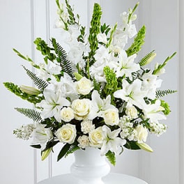 Large white arrangement of lilies, roses, and carnations in a white pedestal vase