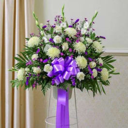 Standing spray of white and purple flowers with a large purple bow on a metal stand