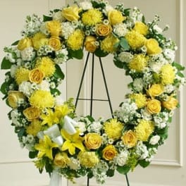 Standing wreath of yellow and white roses, lilies, and mums on an easel with a white ribbon.