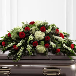 Red and white casket spray with roses and white blooms draped over a bronze casket
