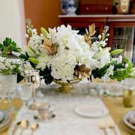 White floral centerpiece in a gold bowl on a dining table
