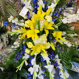 Large standing floral spray with yellow lilies, white blooms, and blue flowers