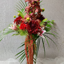 Tall floral arrangement with red and pink blooms in a clear glass vase