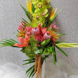 Tall tropical bouquet with green orchids and pink protea in a white vase