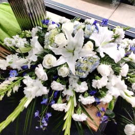 White lilies and roses with blue accents in a large casket spray