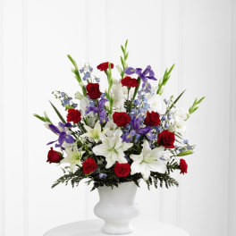 Tall red, white, and blue arrangement with lilies, roses, carnations, and iris in a white urn