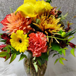 Bright mixed bouquet in a clear glass vase with yellow, peach, and coral blooms.