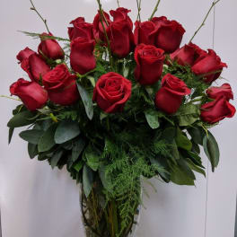 Red roses arranged in a clear glass vase with greenery