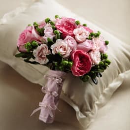 Hand-tied bouquet of pink roses and spray roses with green berries, wrapped in pink ribbon.