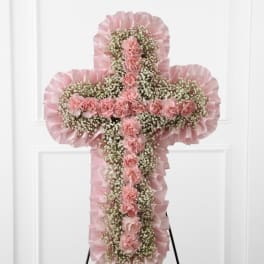 Standing pink cross spray with carnations and baby’s breath on a metal easel.