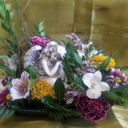Floral arrangement with an angel figurine and mixed blooms in a low container