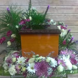 Casket surrounded by white and purple floral sprays