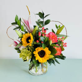 Mixed bouquet with sunflowers, lilies, and pink blooms in a glass vase