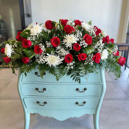Red roses and white daisies arranged on a light blue dresser