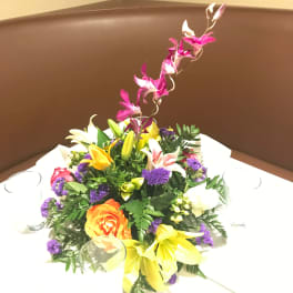 Colorful floral centerpiece in a low arrangement with a tall orchid stem