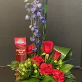 Red roses and blue flowers arranged in a low basket with a tall accent stem