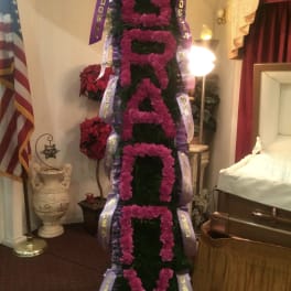 Tall funeral spray with pink flowers and purple ribbons in a room