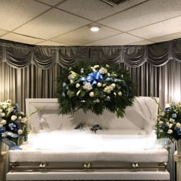 White casket with blue and white floral sprays in a funeral room