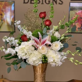 Tall floral arrangement with white blooms, red roses, and pink lilies in a gold vase
