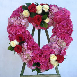 Heart-shaped floral wreath of pink hydrangeas and red and white roses on a stand