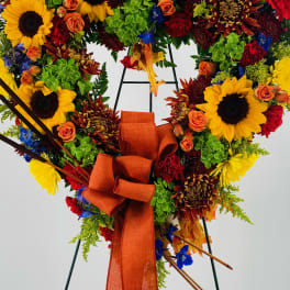Heart-shaped floral wreath with sunflowers, roses, and an orange ribbon on an easel