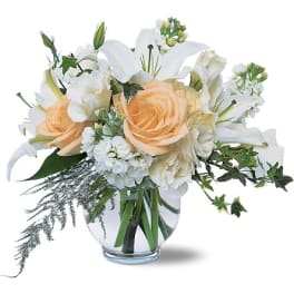 Peach roses and white lilies in a clear glass vase