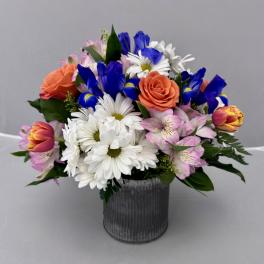 Mixed bouquet of daisies, roses, tulips, and alstroemeria in a metal vase