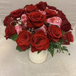 Red roses arranged in a white striped vase with pink heart decorations