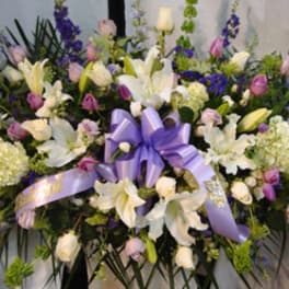 Large floral spray with white lilies, purple flowers, and a lavender ribbon