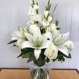 White lilies and roses arranged in a glass vase with a ribbon