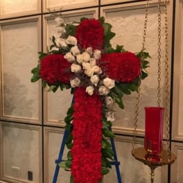 Red floral cross on a stand with white roses and greenery