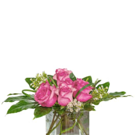 Pink roses arranged in a clear glass vase with greenery