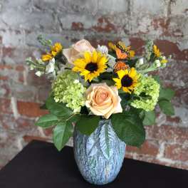 Peach roses and yellow sunflowers in a blue vase with butterfly accents
