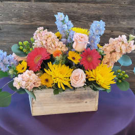 Mixed bouquet in a wooden box with pink, yellow, blue, and red flowers