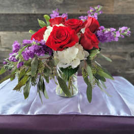 Mixed arrangement of red roses, white hydrangea, and purple flowers in a clear glass vase
