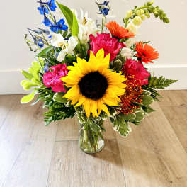 Colorful bouquet with a sunflower, gerbera daisies, and lilies in a glass vase