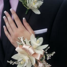 White floral corsage and boutonniere on a black suit with pink ribbon